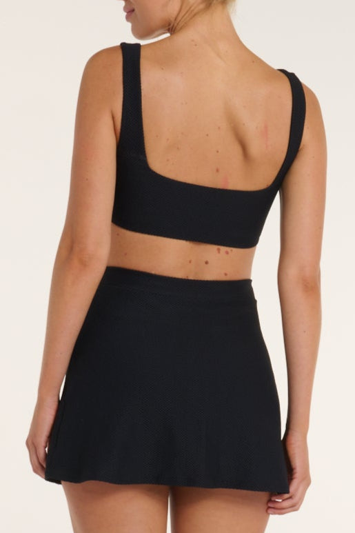 Person wearing a black sports bra and skirt set on a white background