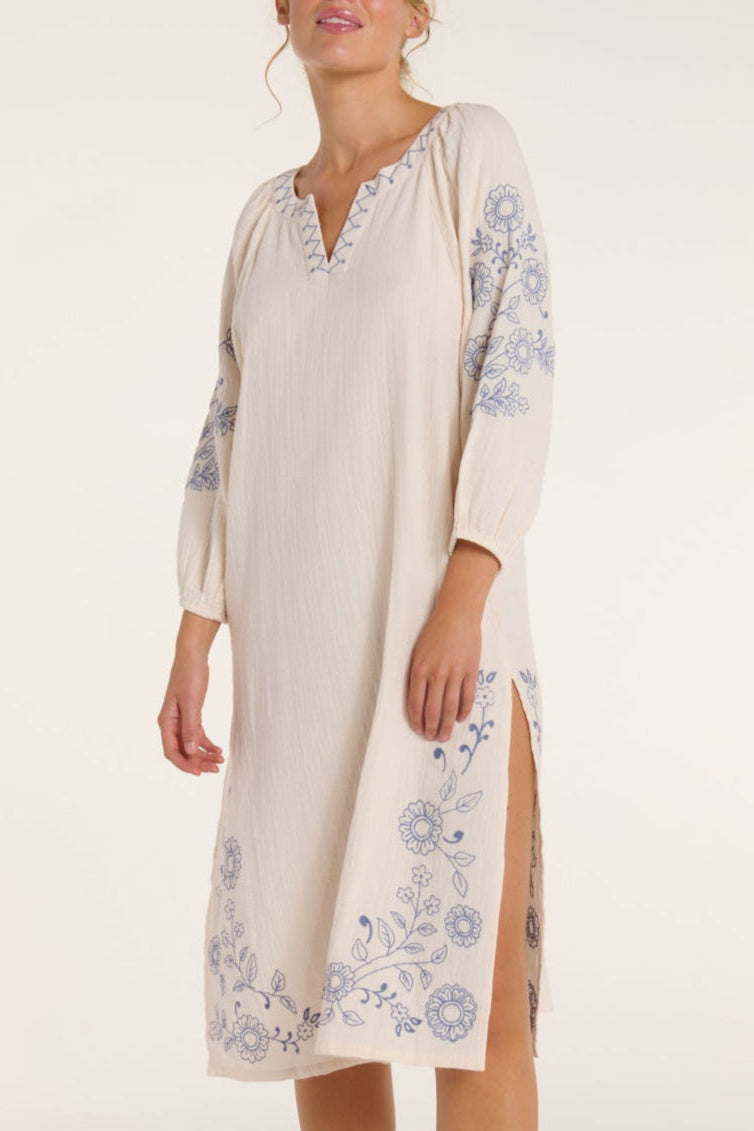 Woman wearing a beige dress with floral embroidery on a white background