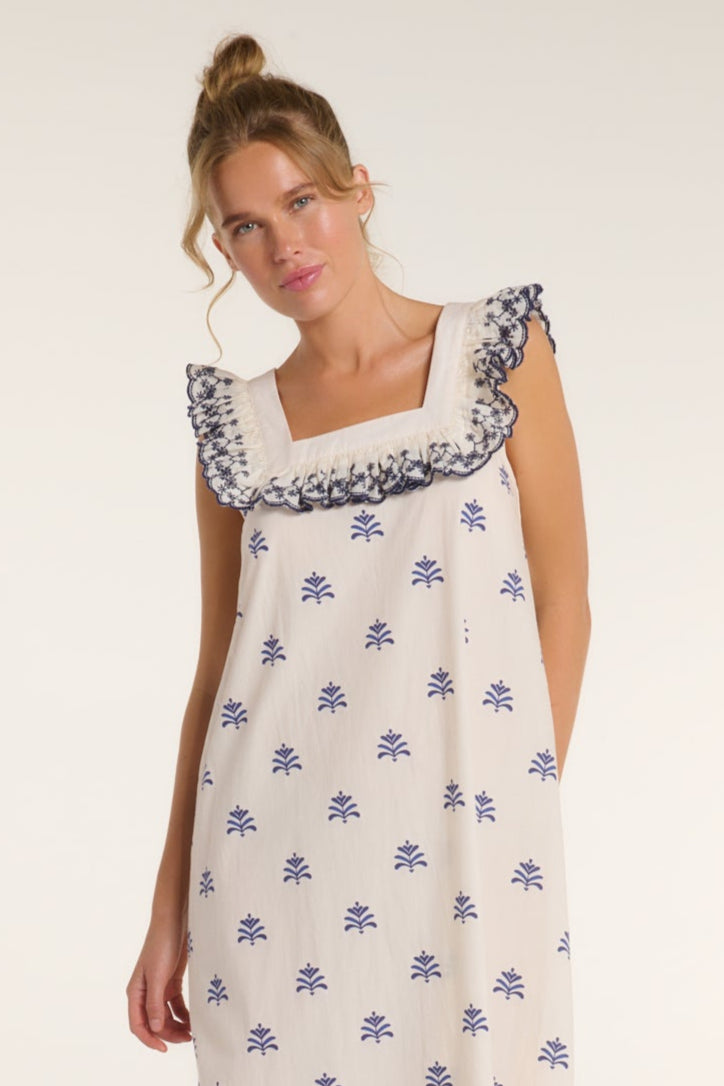 Woman wearing a white dress with blue floral patterns on a plain background