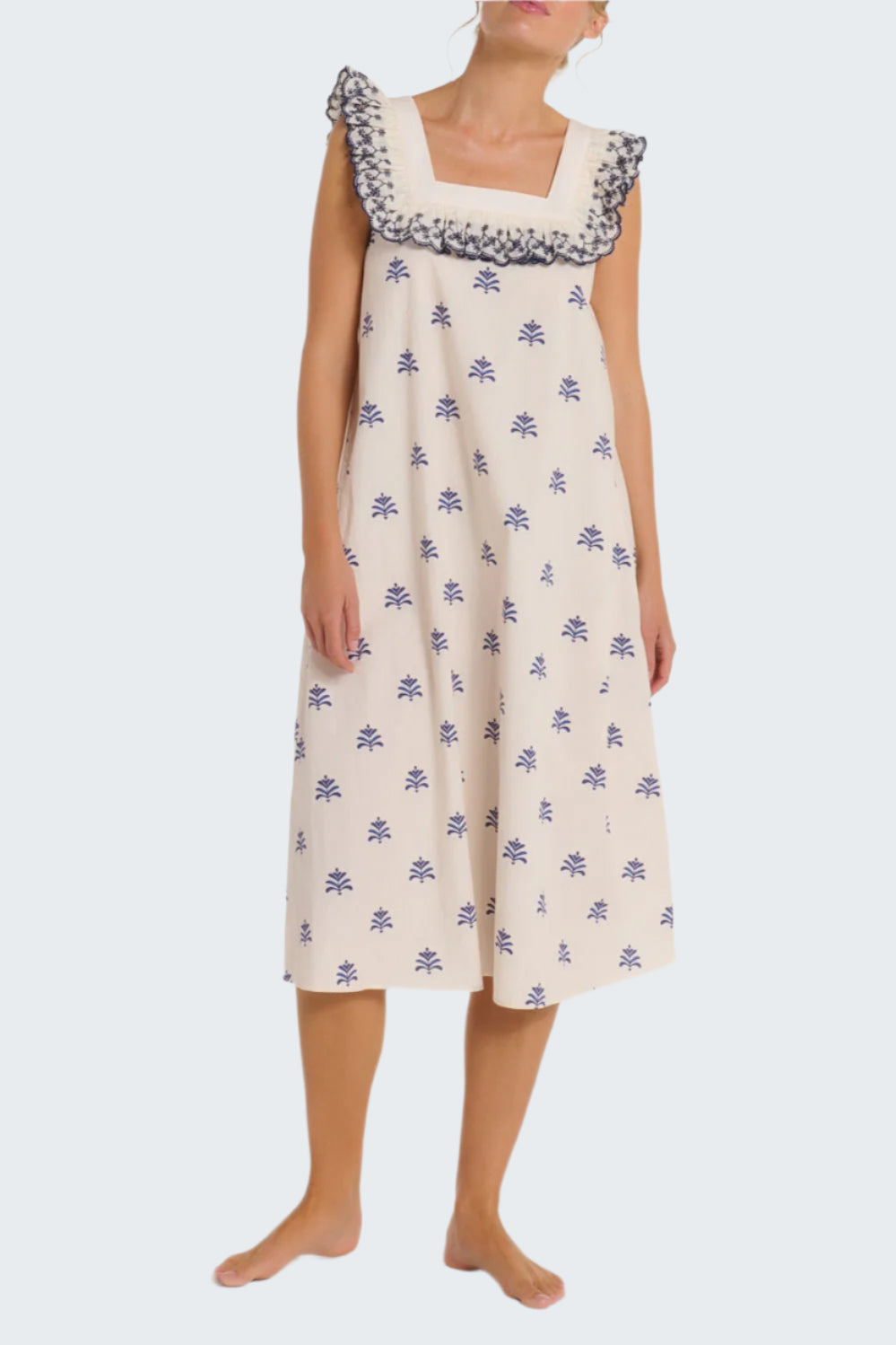 Woman wearing a white dress with blue floral patterns on a plain background