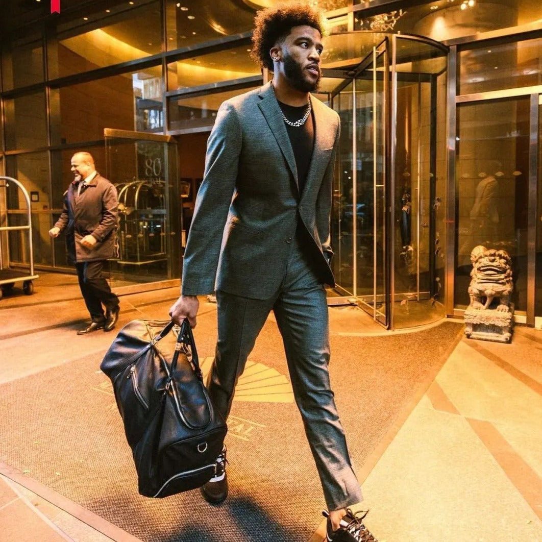 Man in a suit with a suitcase exiting a building at night.