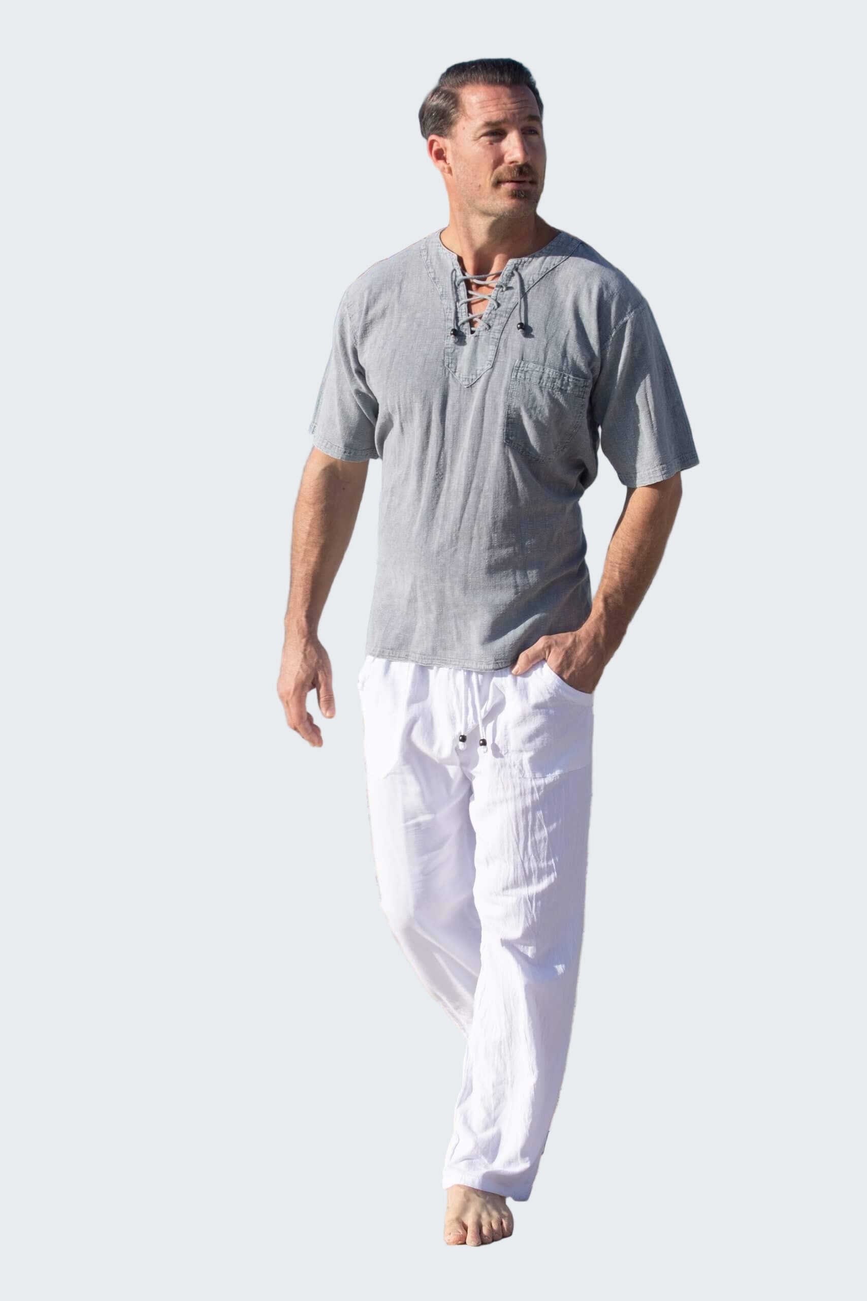Man walking on a beach wearing a gray shirt and white pants.