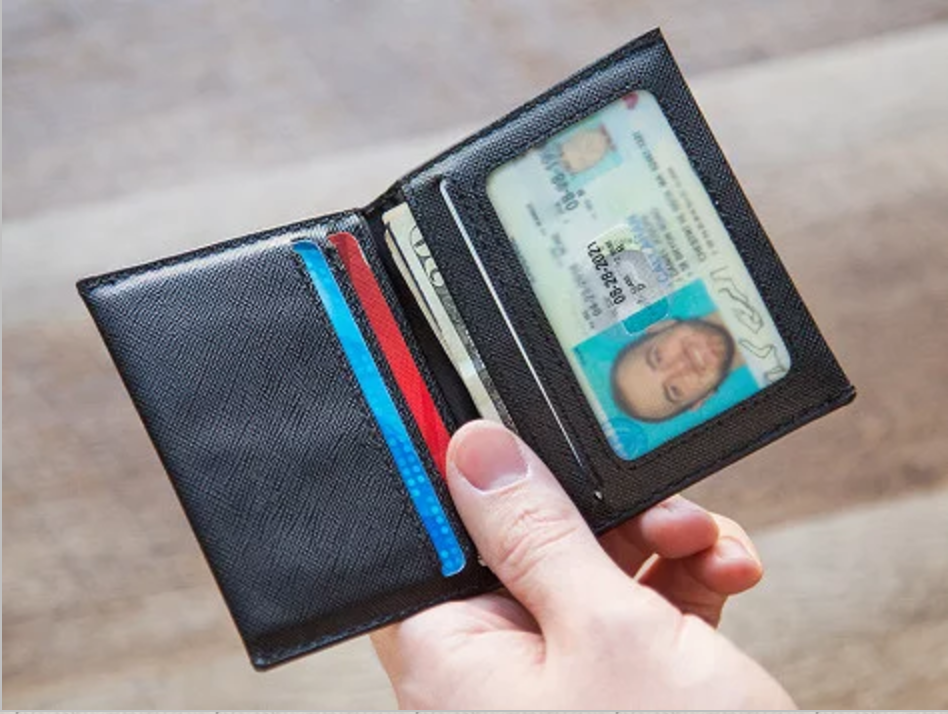 Black wallet with a card and ID held by a hand on a wooden surface