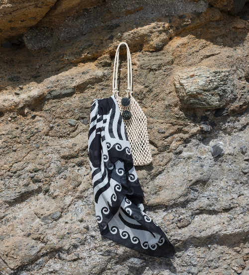 Black and white patterned scarf draped over a beige woven bag on a rocky surface
