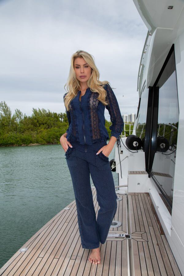Woman standing on a dock by a yacht with water and greenery in the background