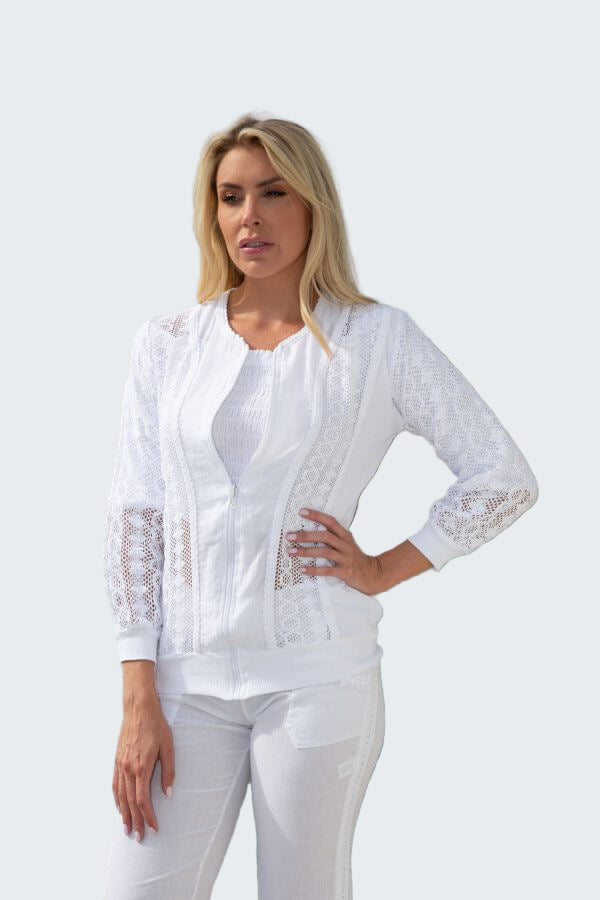 Woman wearing a white lace top and pants by a body of water with trees in the background
