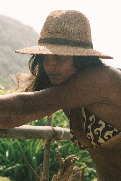 Woman wearing a wide-brimmed hat and patterned swimsuit in a natural setting