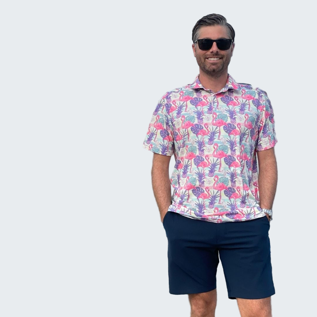 Man wearing a colorful patterned shirt and sunglasses standing by a marina.