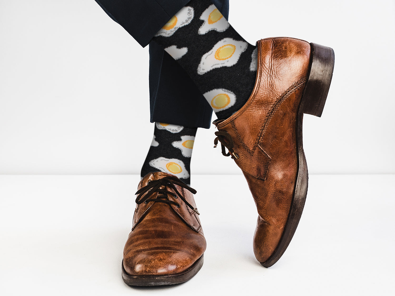 Brown dress shoes with black laces worn with socks featuring egg designs on a white background