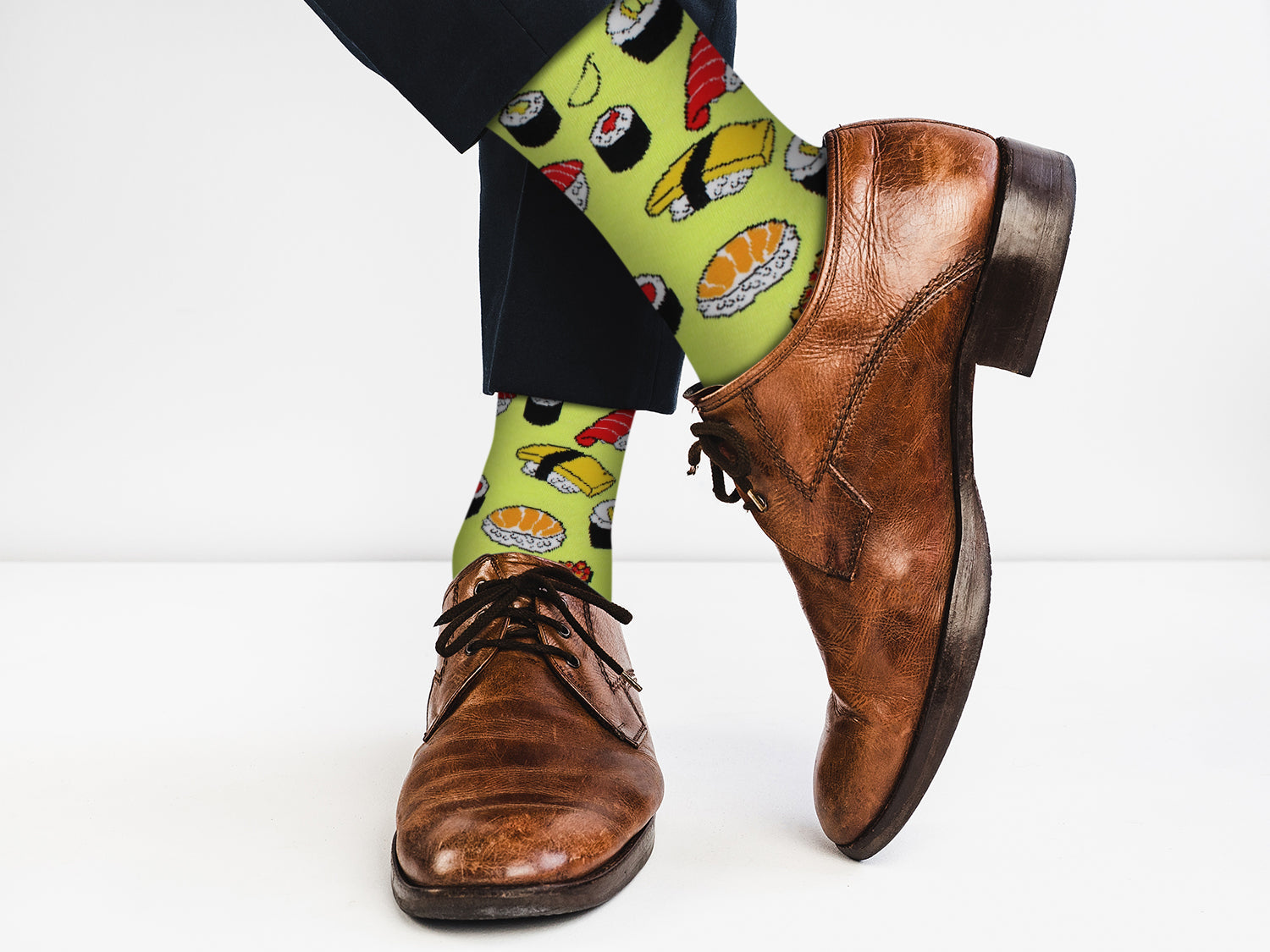 Person wearing brown dress shoes and colorful sushi-themed socks on a white background