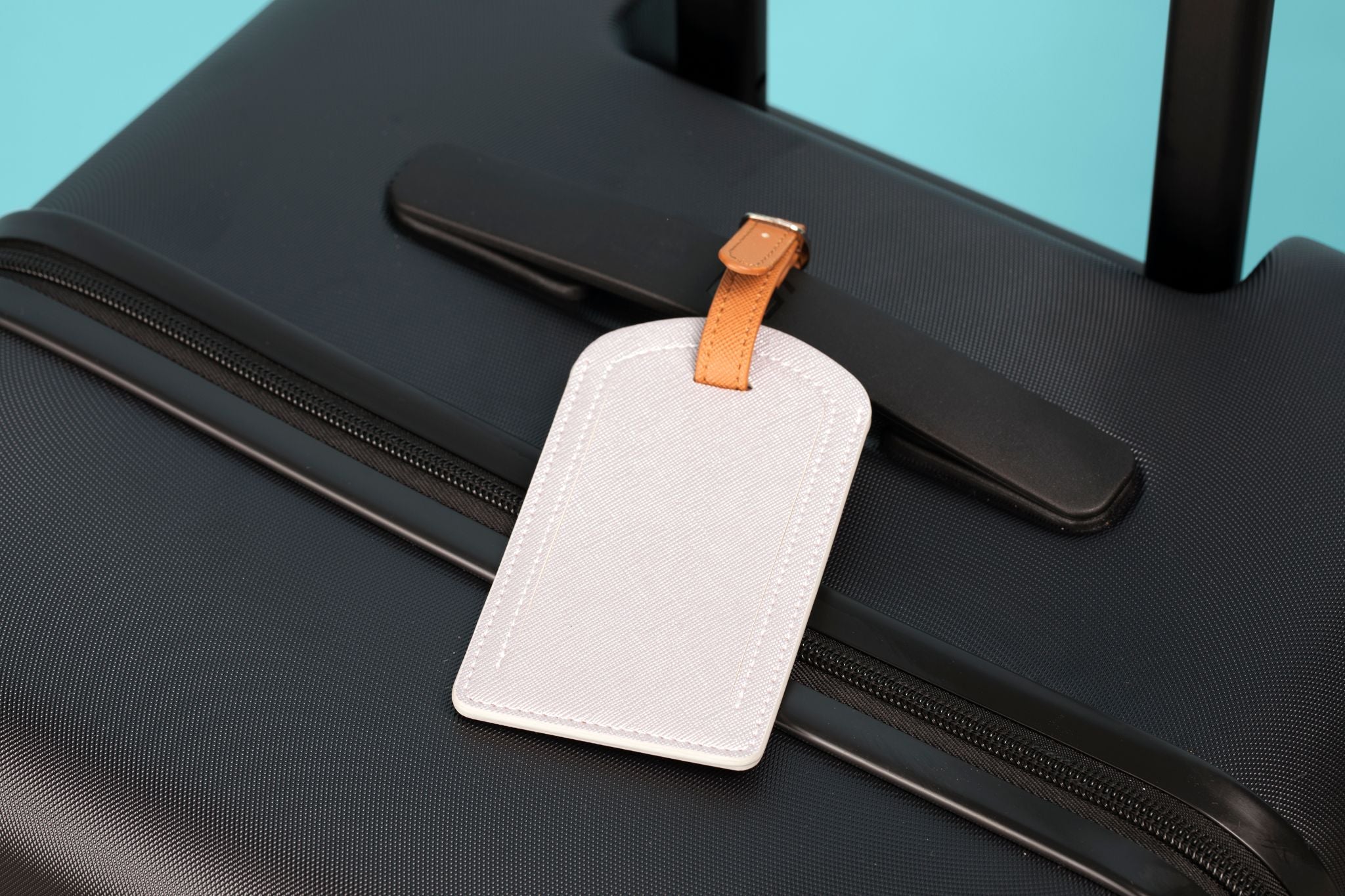 Luggage tag attached to a black suitcase with a turquoise background