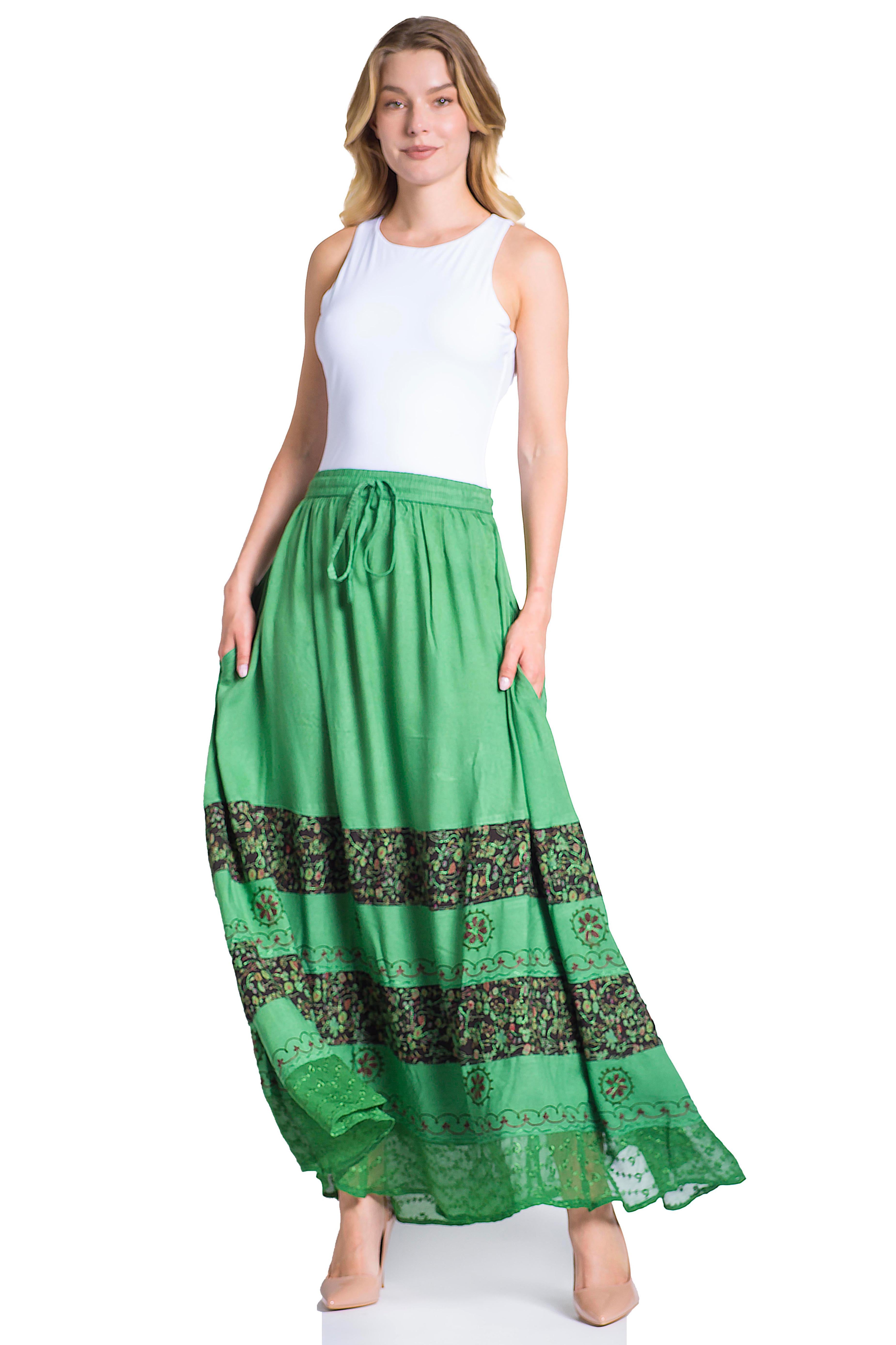 Woman wearing a white sleeveless top and green maxi skirt with patterned hem on a white background