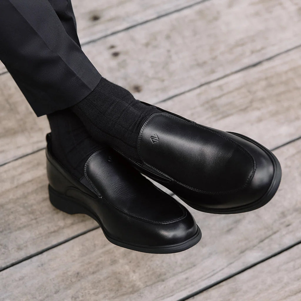 Black leather shoes worn with black pants on a wooden floor