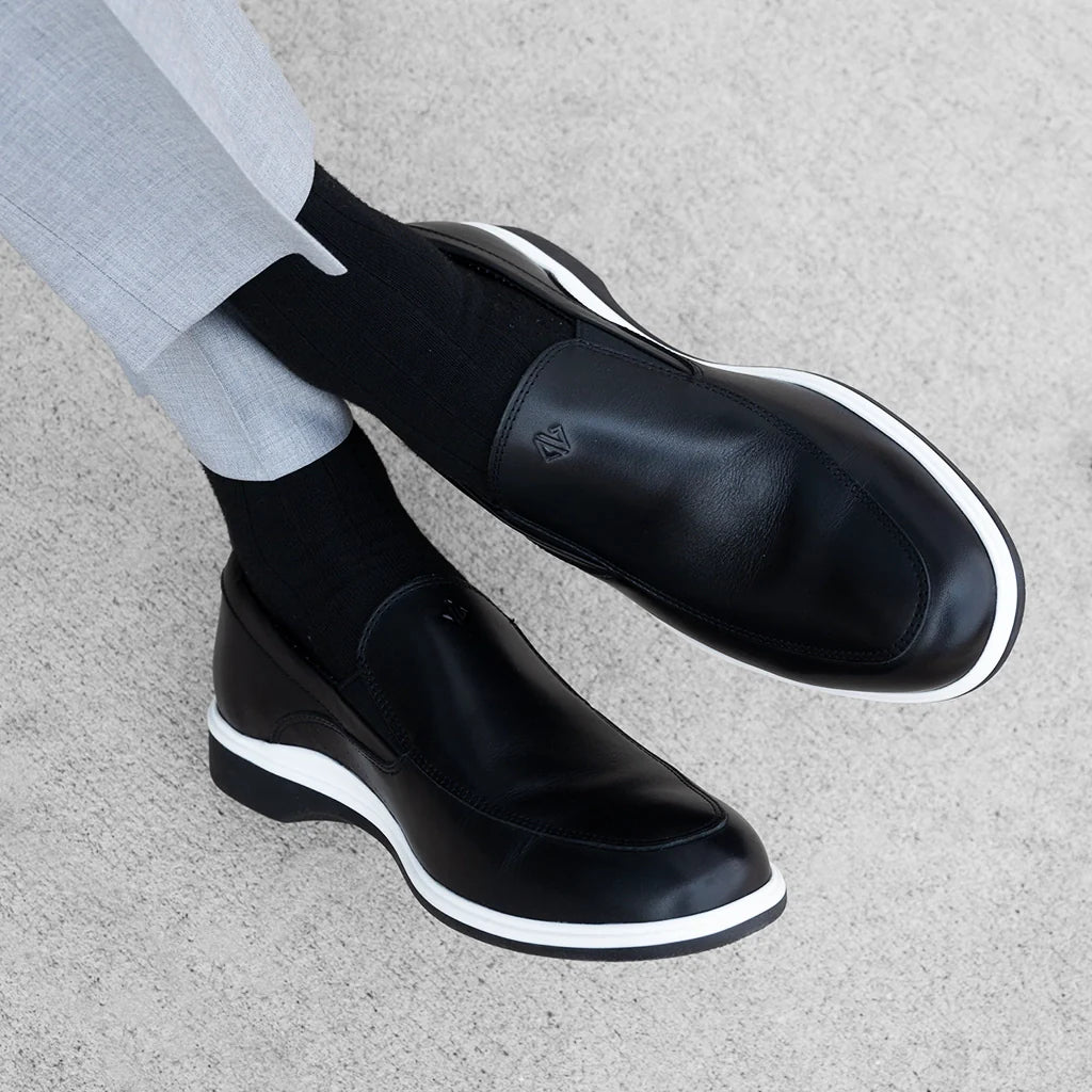 Black leather shoes with white soles worn by a person on a gray surface