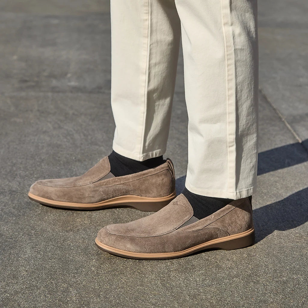 Brown suede loafers worn with beige pants on a gray pavement.