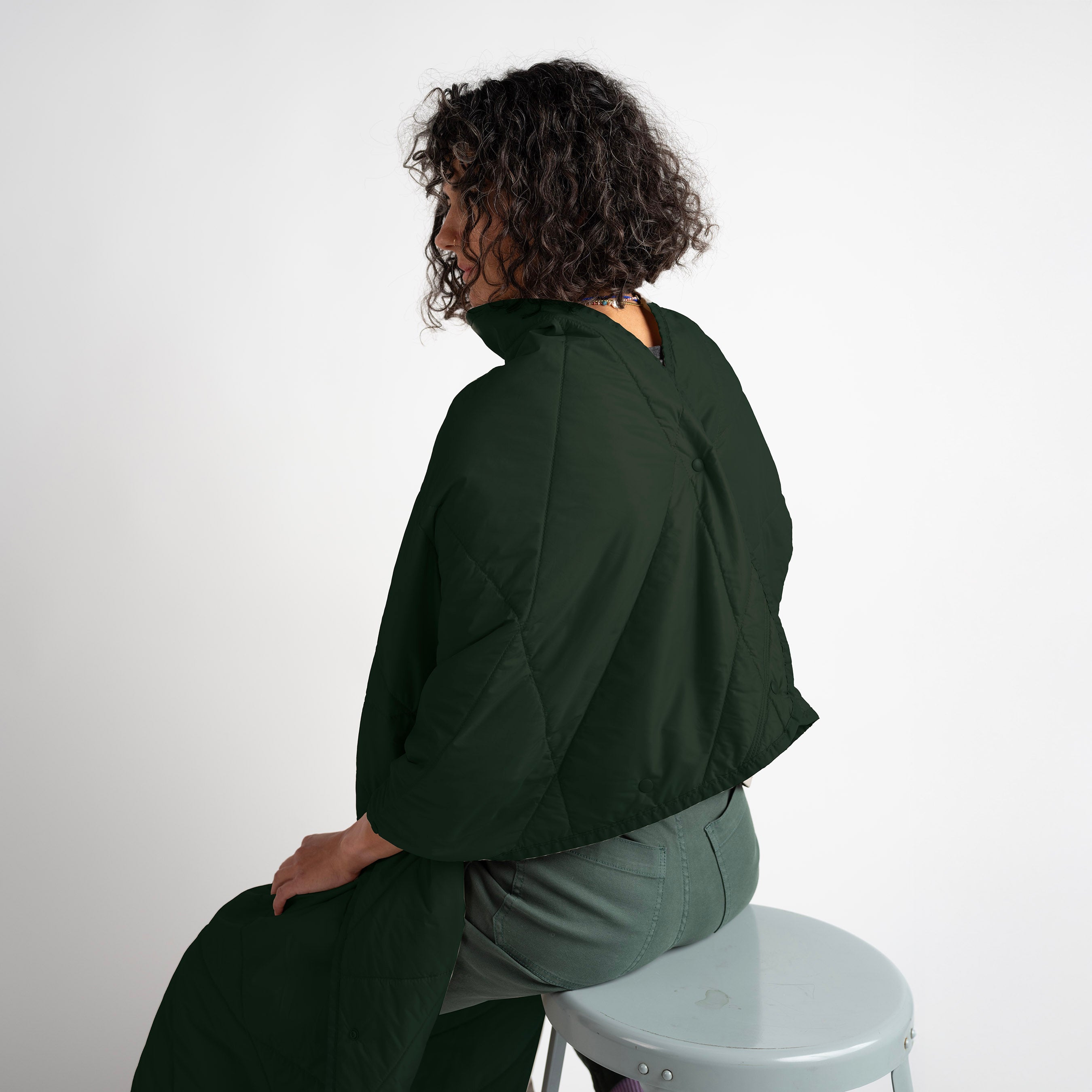Person wearing a green jacket sitting on a white stool against a white background