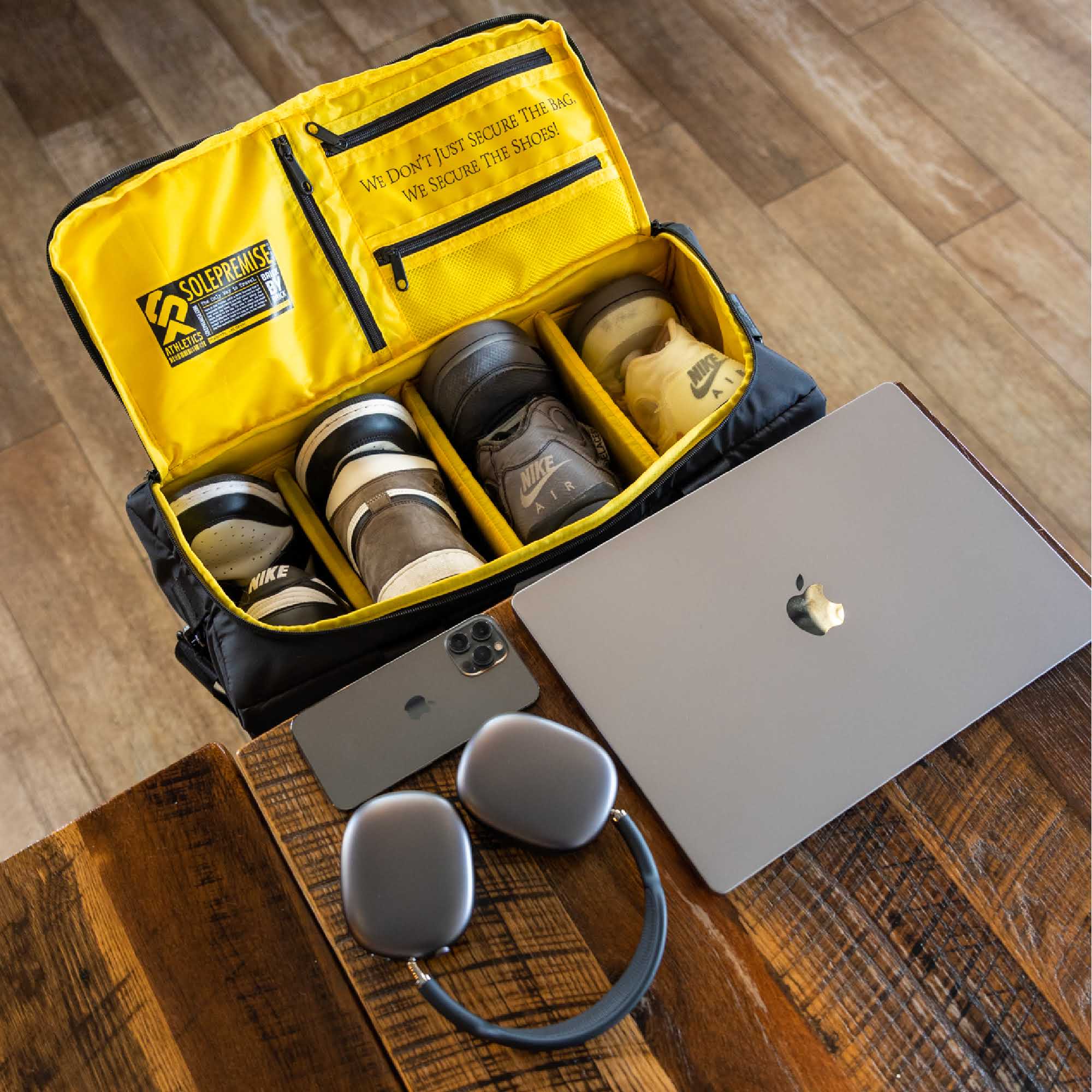 Yellow shoe bag with shoes on a wooden floor, next to a laptop and headphones.