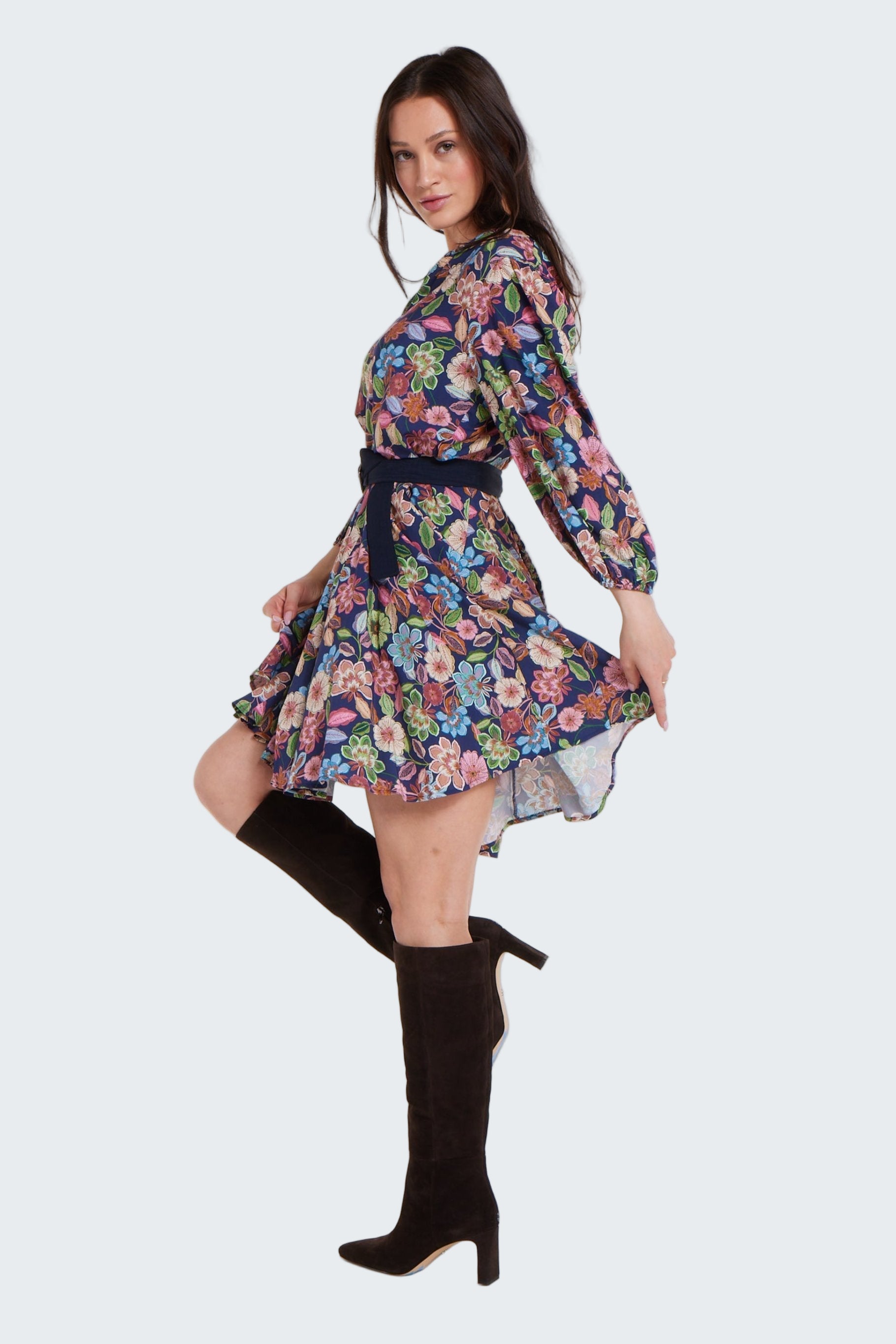 Woman wearing a floral dress with long sleeves and knee-high black boots on a white background
