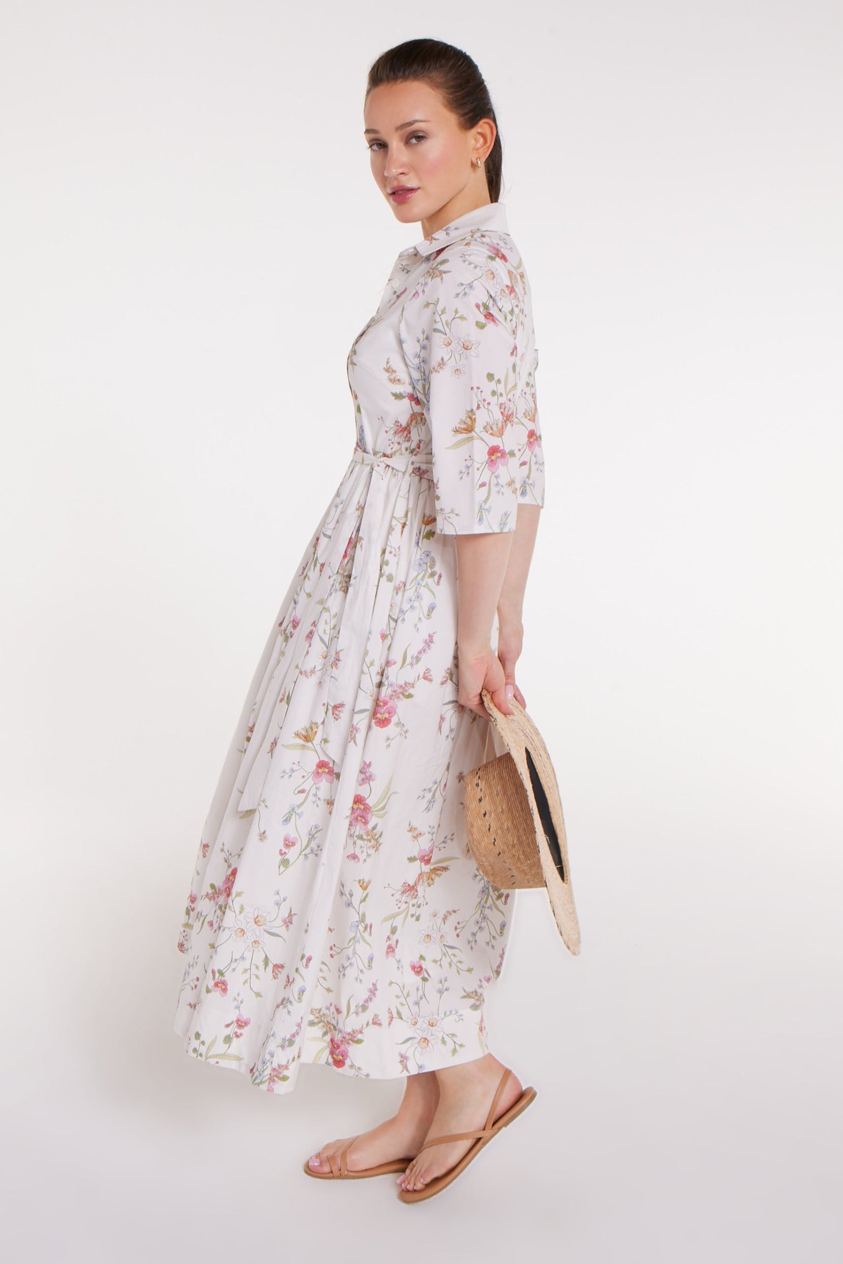 Woman wearing a floral dress holding a straw bag on a white background