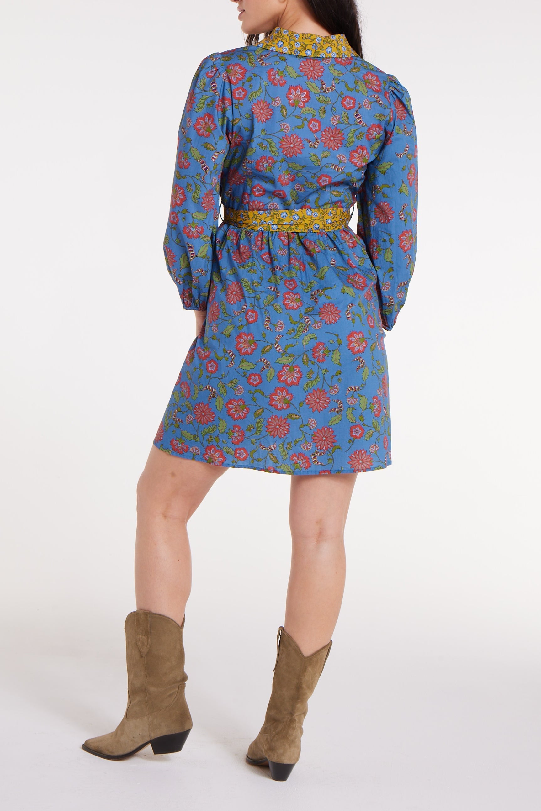 Woman wearing a blue floral dress with a belt and brown boots on a white background