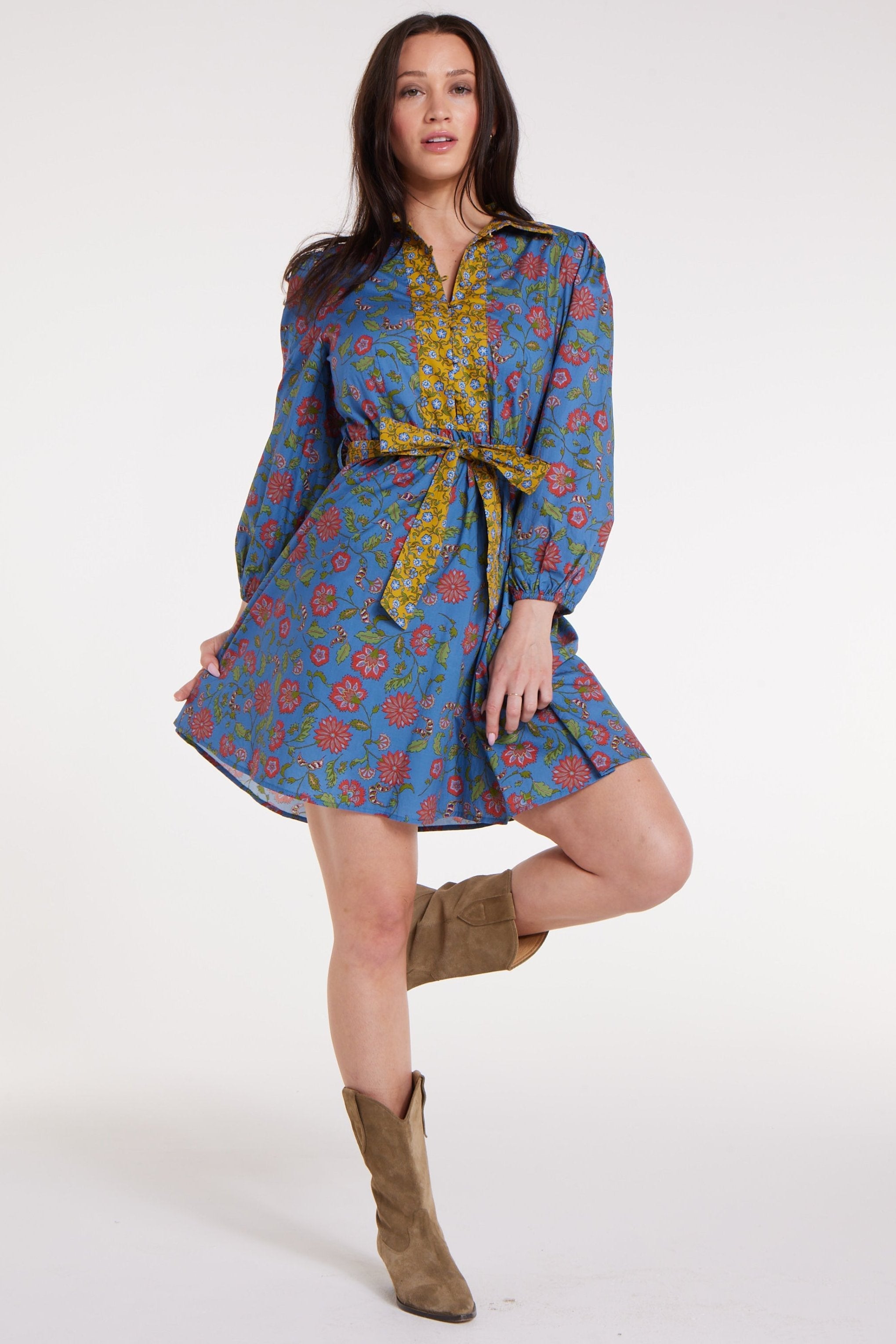 Woman wearing a colorful patterned dress with a belt and brown boots on a white background