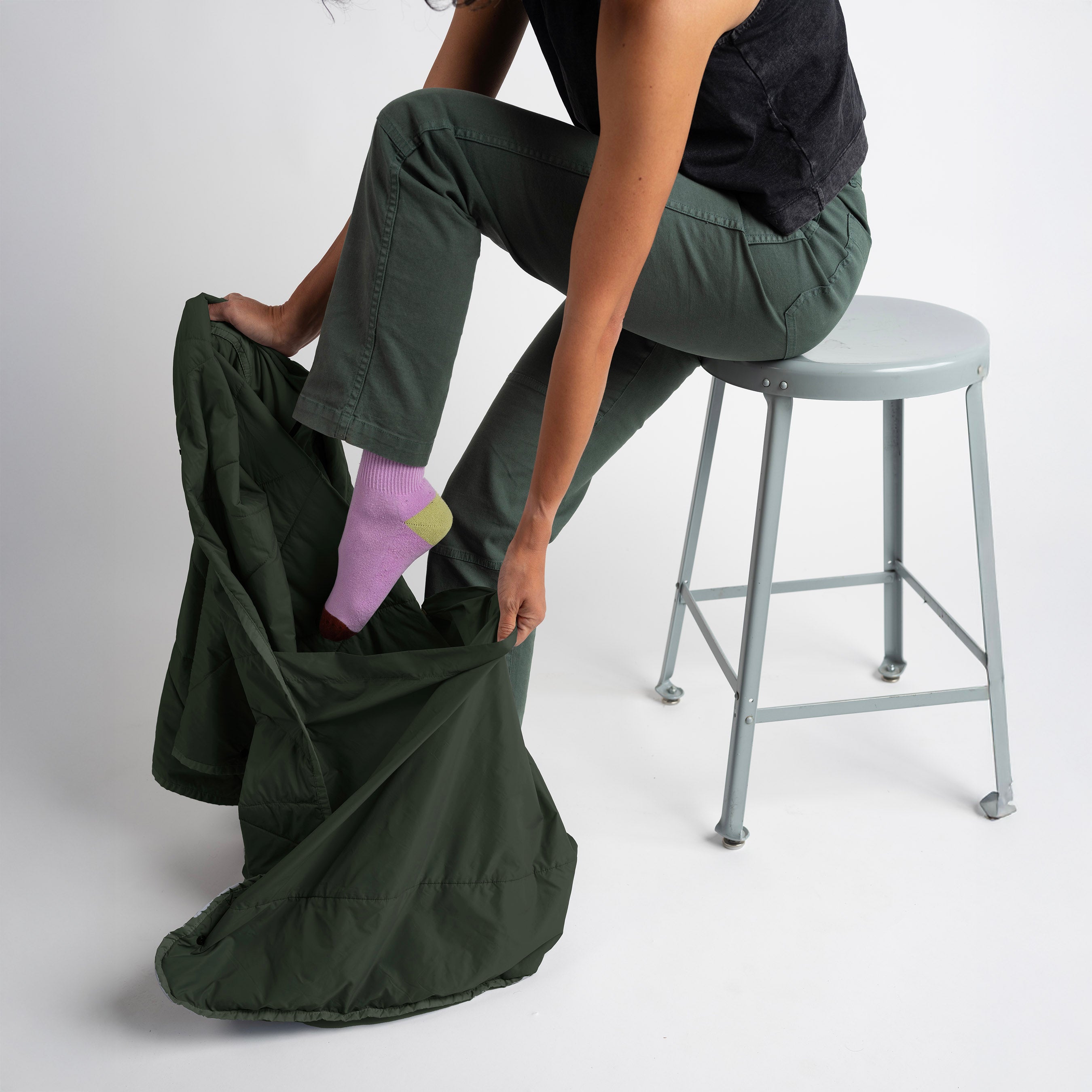 Person sitting on a stool with a green laundry bag filled with clothes on a white background