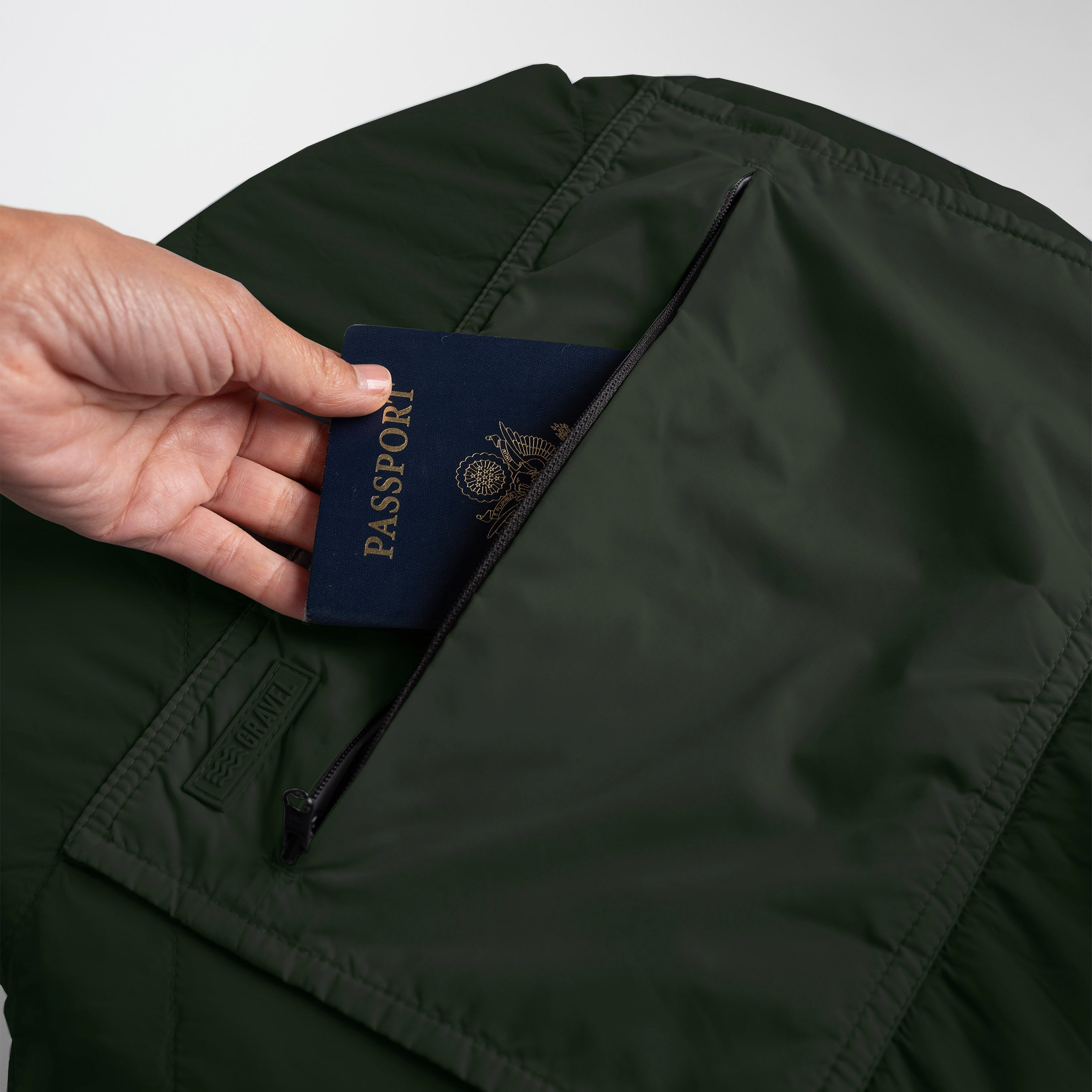 Hand placing a passport into a dark green jacket pocket.