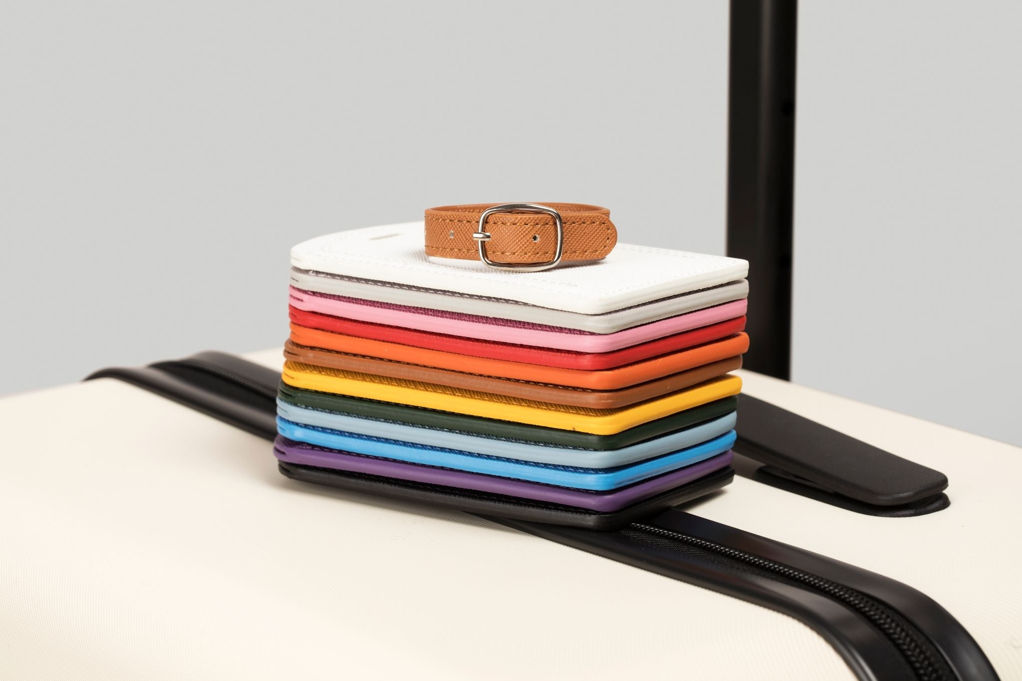 Stack of colorful folded fabrics with a brown belt on top, placed on a black stand against a light gray background.