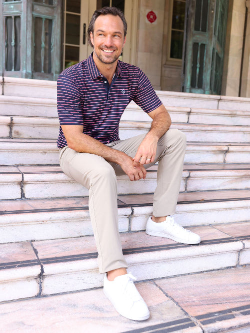 Man sitting on steps wearing a striped polo shirt, beige pants, and white shoes.