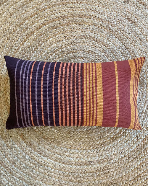 Striped pillow with purple, orange, and red colors on a woven surface