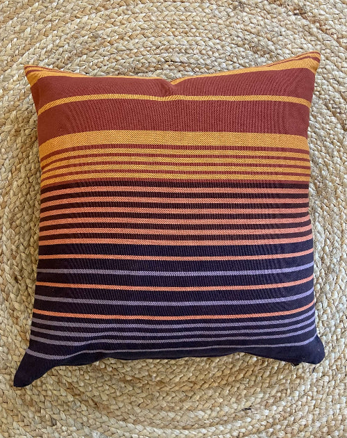 Striped pillow with brown, orange, and purple colors on a woven mat background