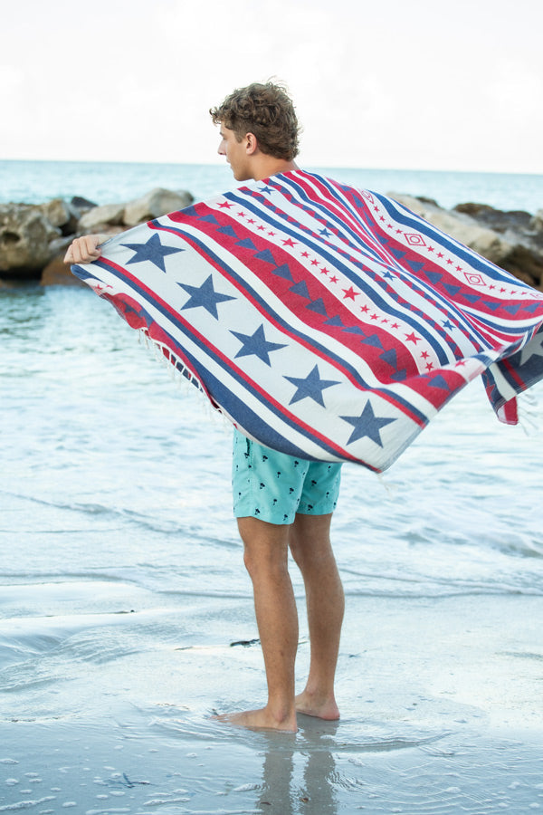 Person holding a red, white, and blue patterned towel on a beach