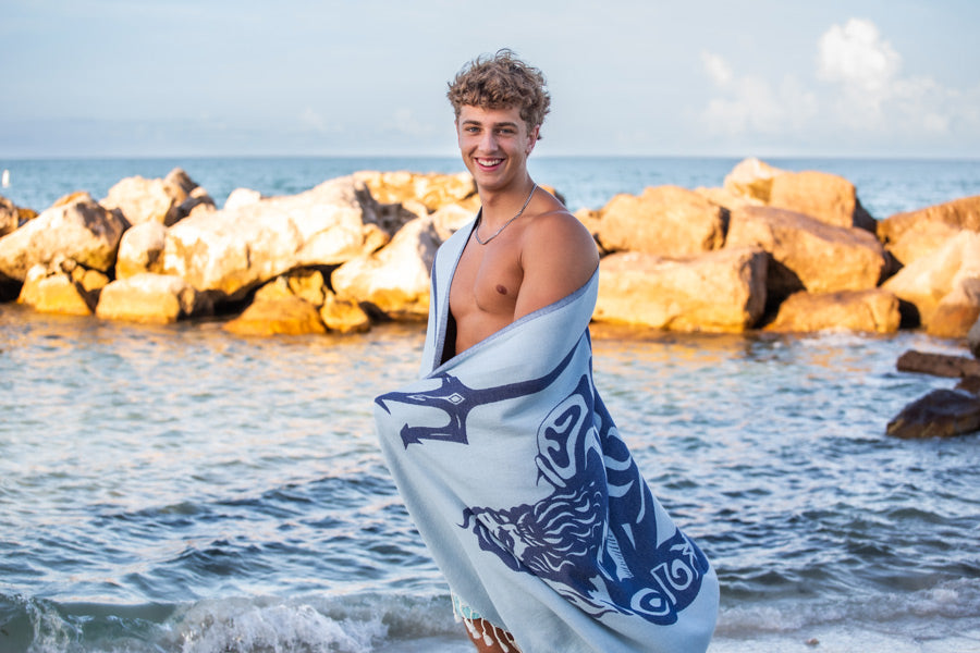 Man holding a towel with a beach scene design, standing on a rocky shoreline.