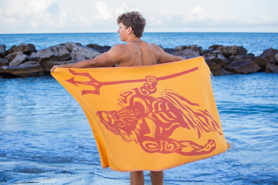 Person holding a yellow towel with a red design by the ocean