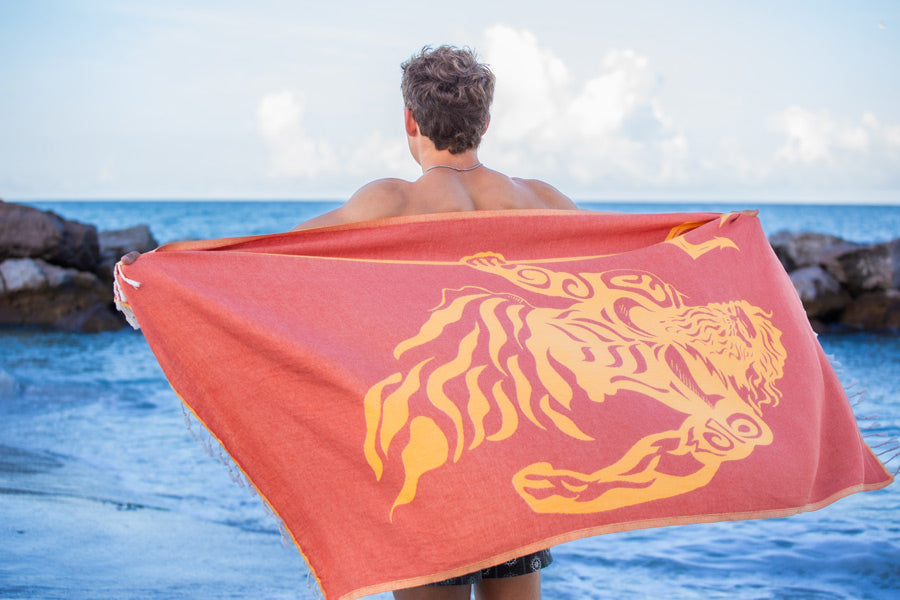 Person holding a red towel with a yellow tiger design by the ocean.