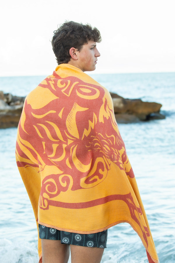 Person wrapped in a yellow and red patterned towel by the ocean