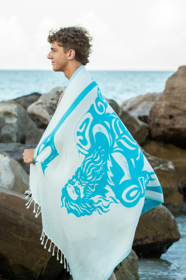 Person holding a beach towel with a blue and white design by the ocean.