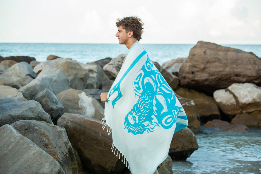 Person wrapped in a towel with a wolf design by a rocky beach