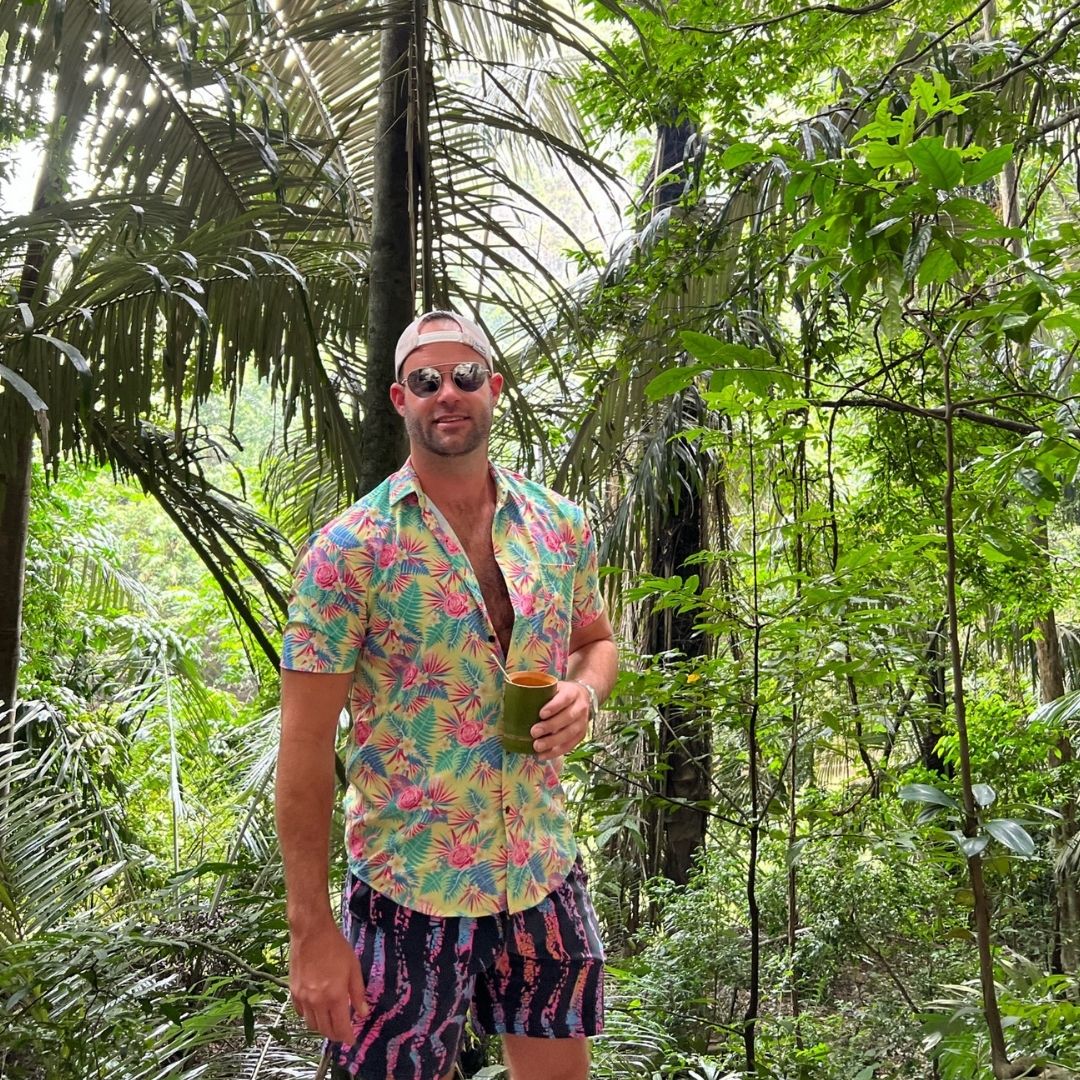 Man in a tropical shirt and shorts standing in a lush green forest