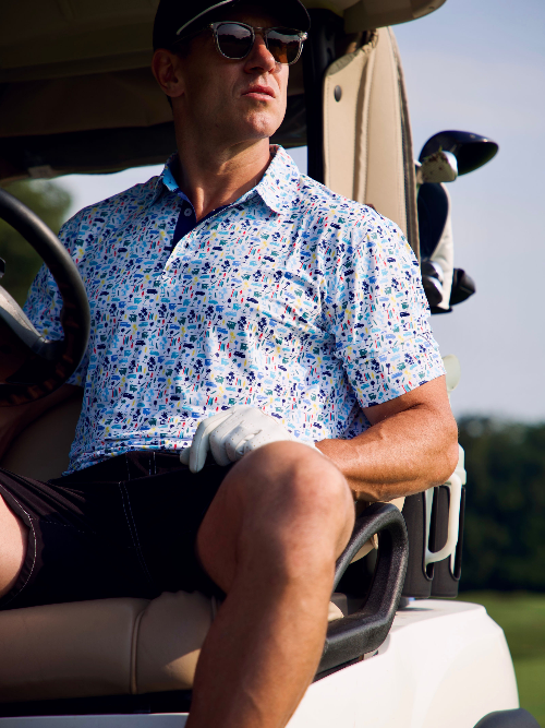 Man sitting in a golf cart wearing a patterned shirt and sunglasses.