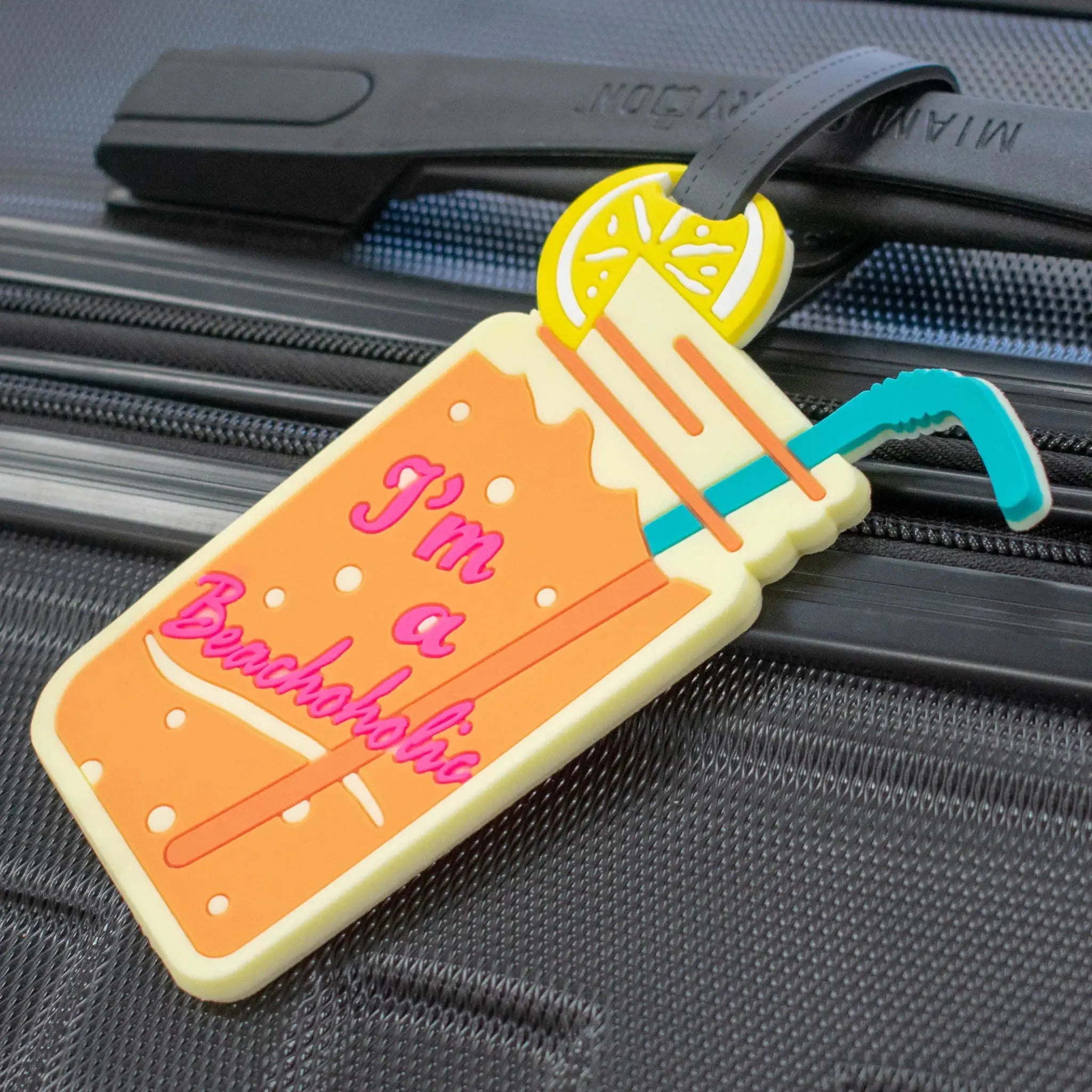 Luggage tag shaped like a cocktail with text 'I'm a Brochoholics' attached to a suitcase.