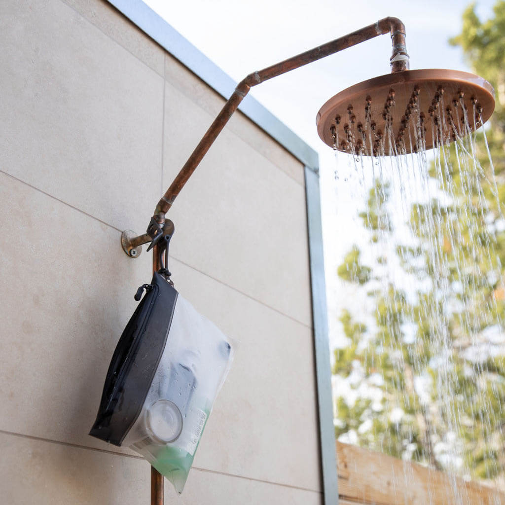 Outdoor shower head with arm attached to a wall, with water flowing.