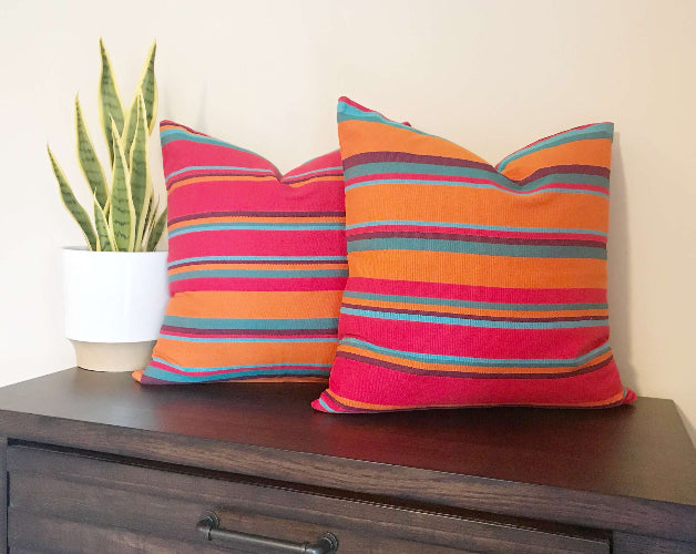 Two colorful striped pillows on a wooden surface with a plant in the background.