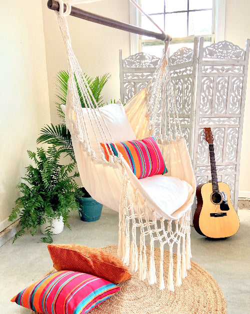 Hanging chair with colorful pillows in a room with plants and a guitar