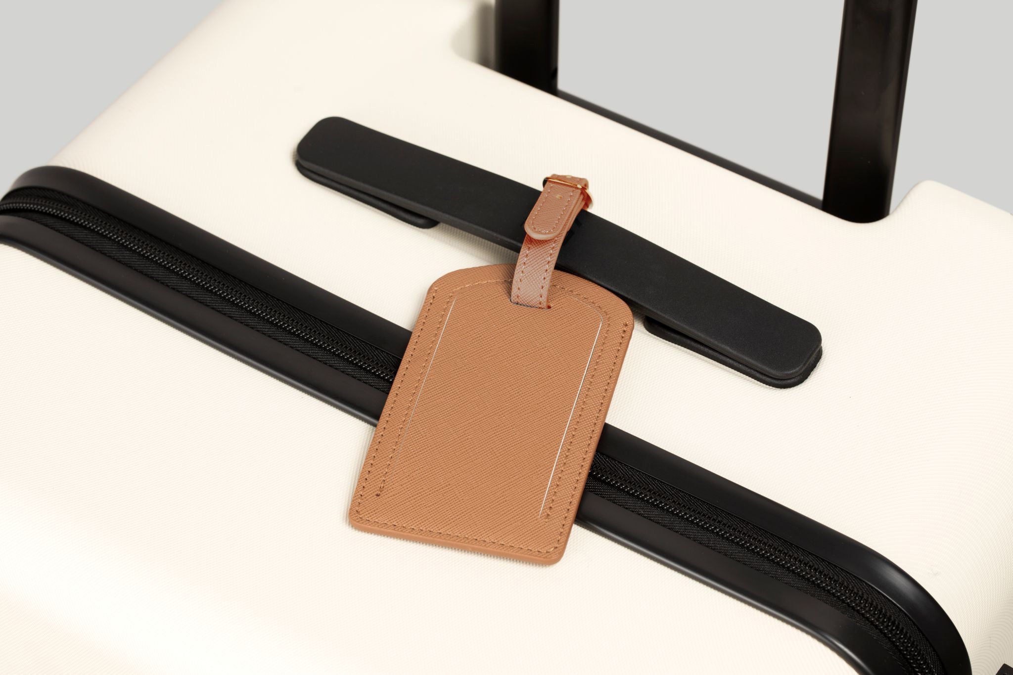 Brown leather luggage tag attached to a black strap on a suitcase.