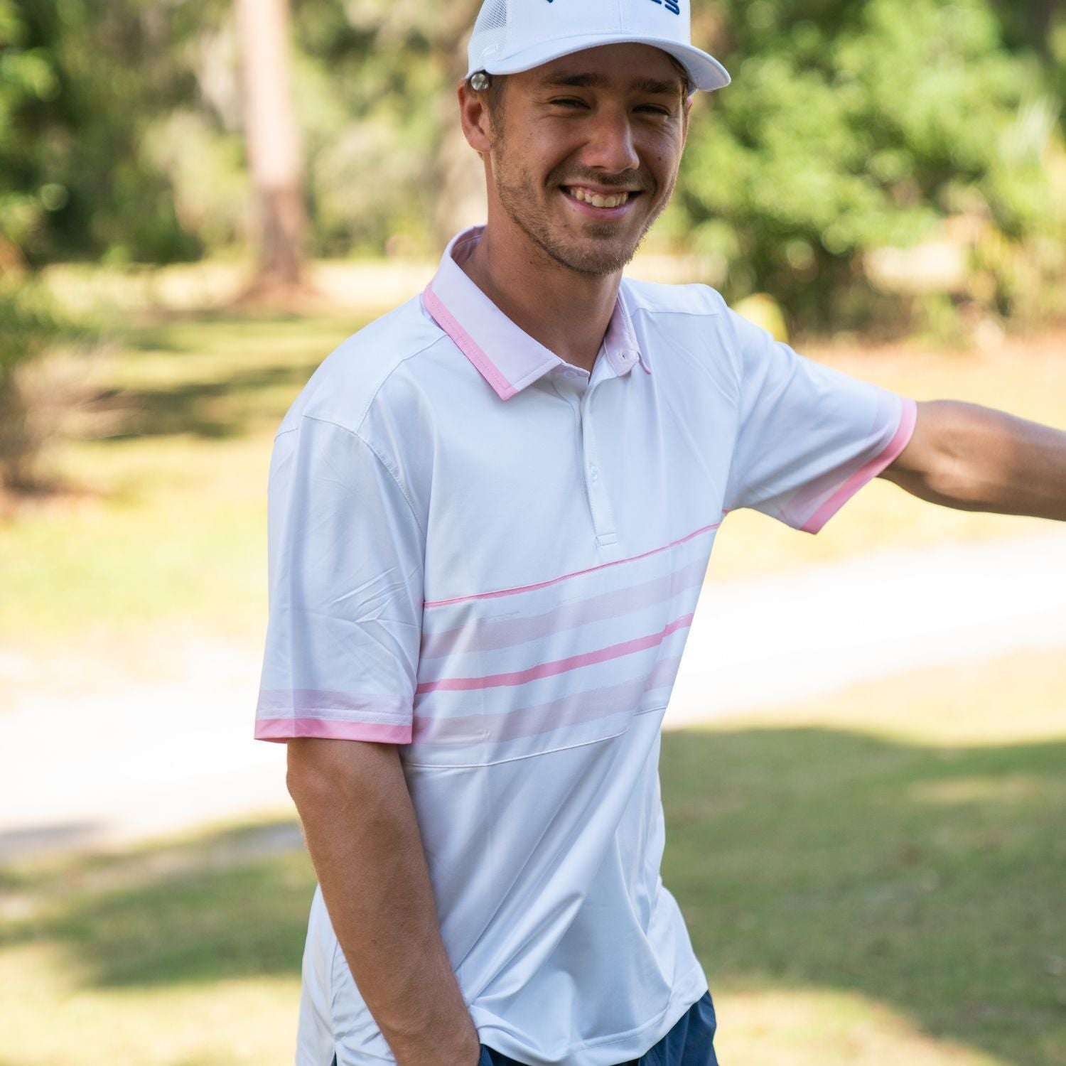Man wearing a white and pink striped polo shirt with a cap in a park setting