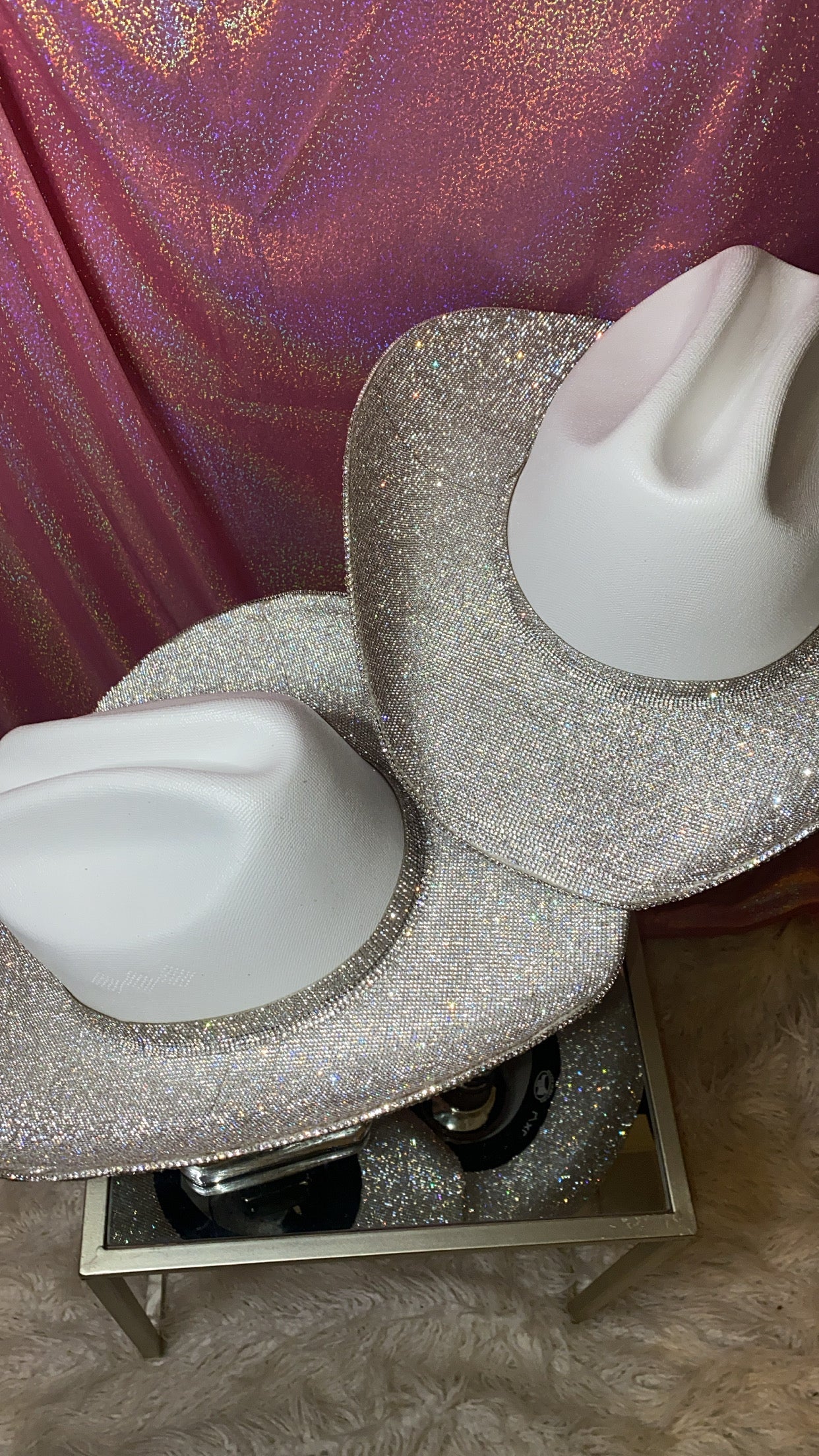 Two glittery white shoes on a stand with a textured pink curtain background