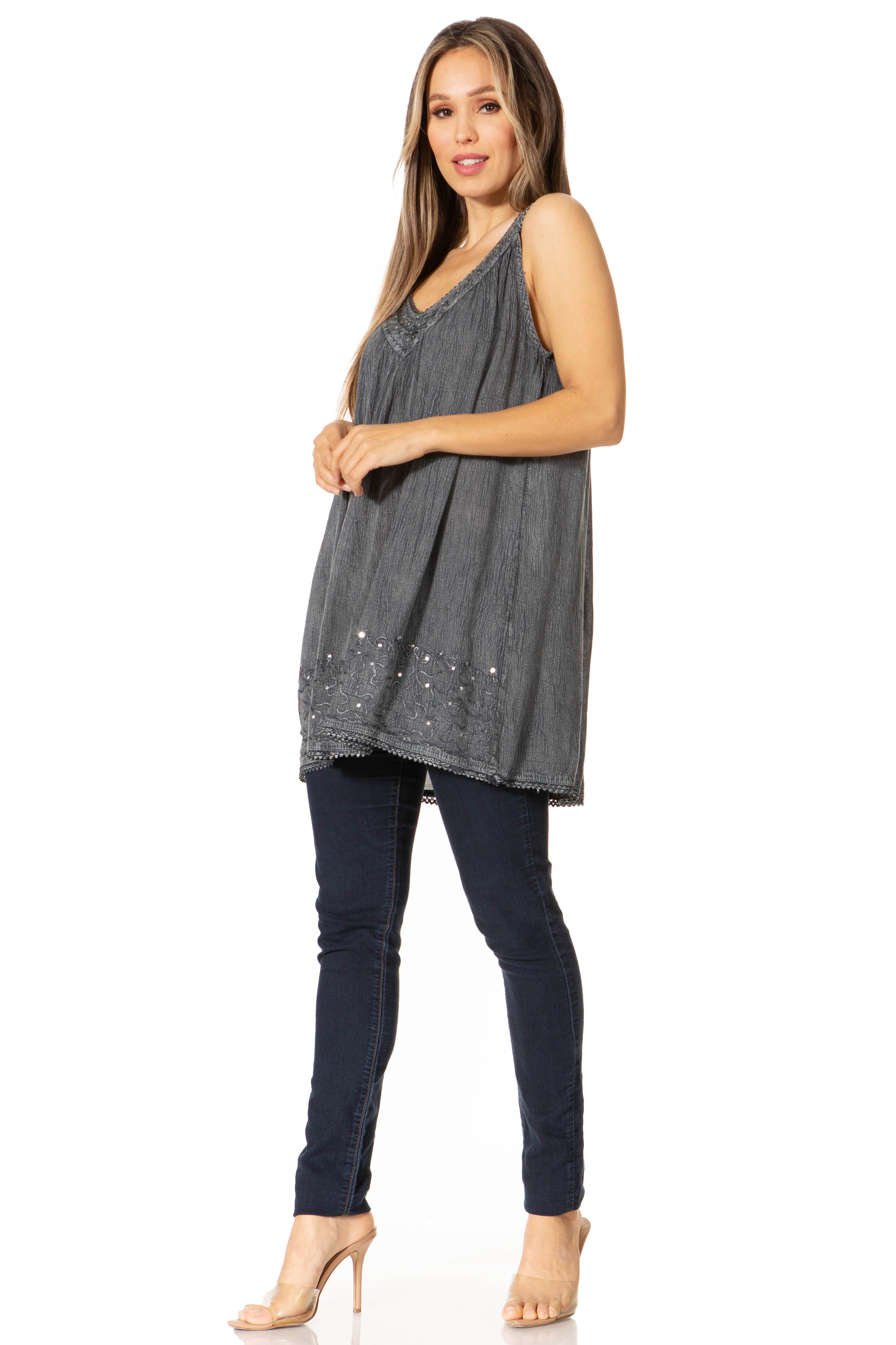 Woman wearing a gray sleeveless top with sequins and dark jeans on a white background