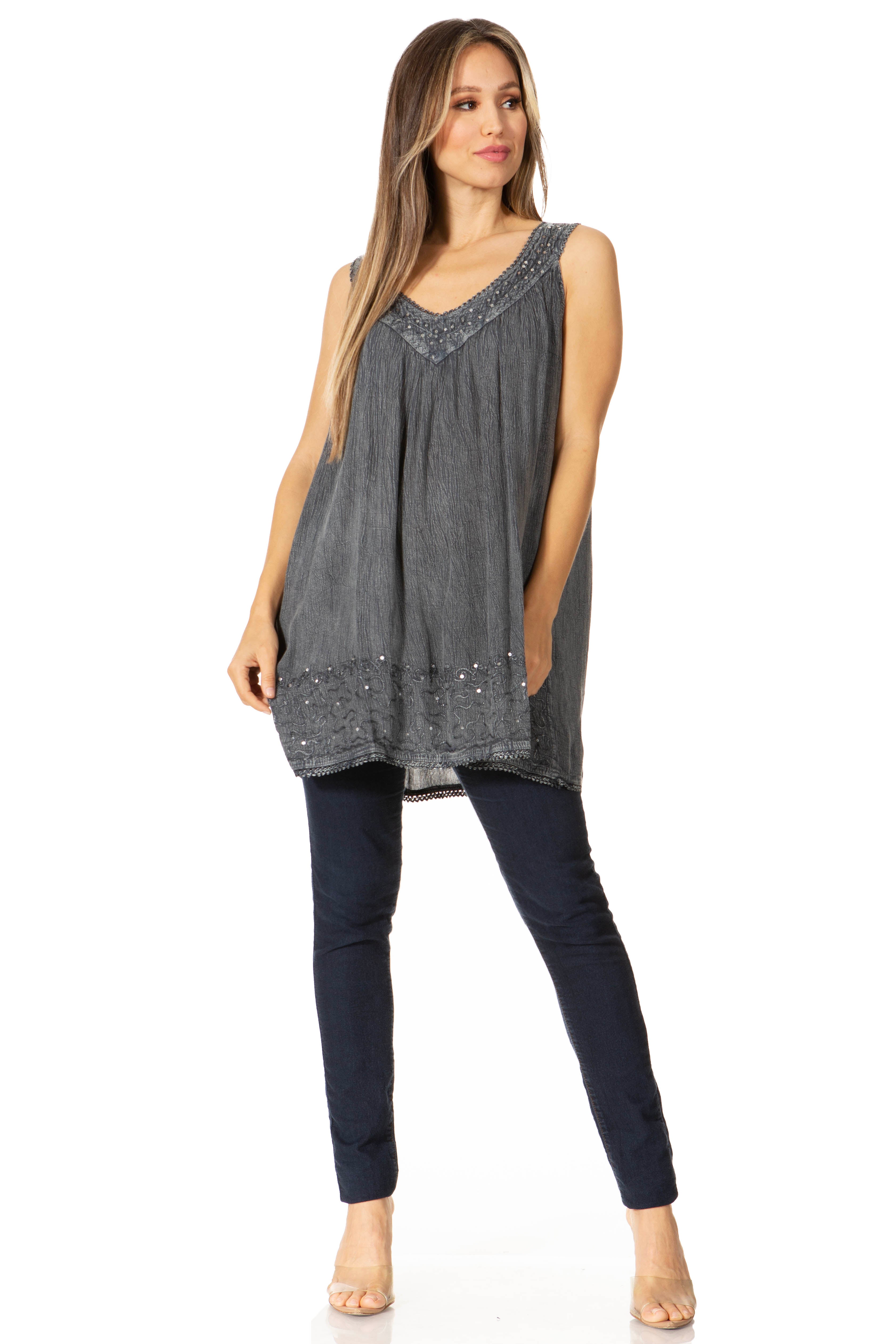 Woman wearing a sleeveless gray top with embellishments and dark pants on a white background
