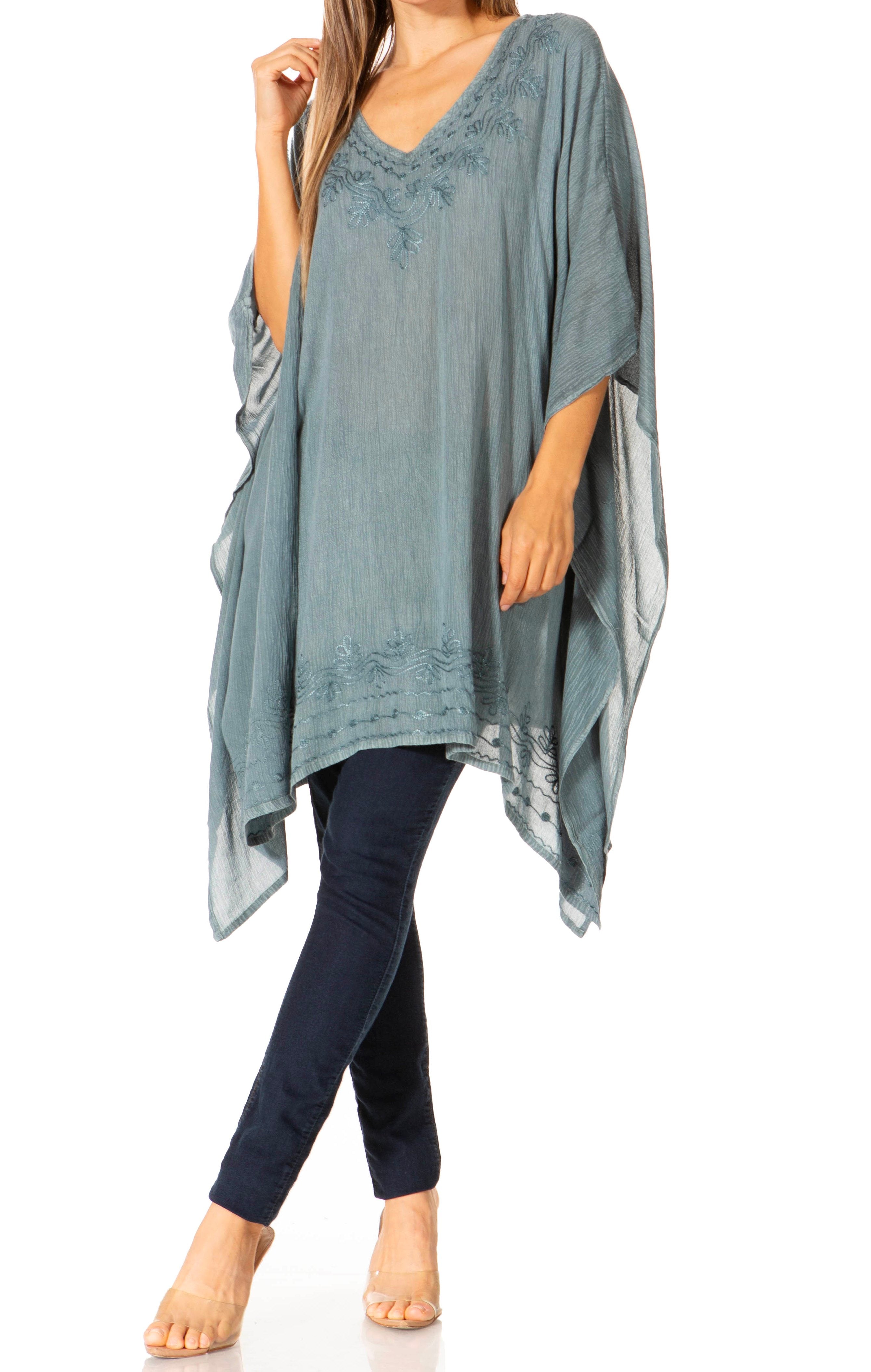 Woman wearing a teal poncho over a blue top and black pants on a white background